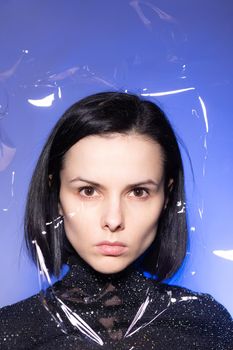 woman with purple lips in a black turtleneck with sequins on a blue background, photo through plastic film. High quality photo