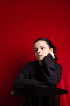 a woman in a black sweater sits at a chair, red background. High quality photo