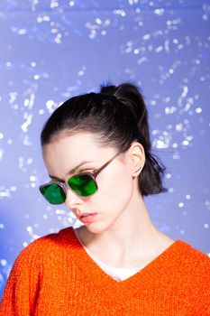 beautiful girl in an orange sweater and green glasses on a blue background. High quality photo