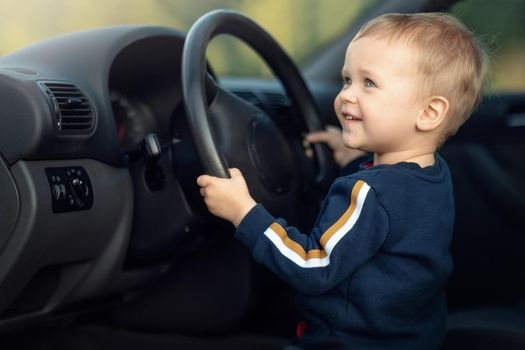 Cute little boy pretending to drive a car sitting behind the steering wheel