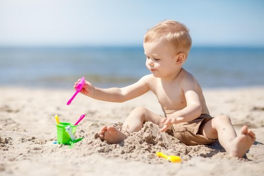 Cute baby boy playing with beach toys. The child neatly puts the toys in the bucket.