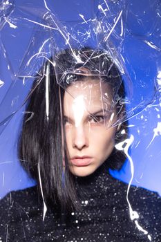 woman with purple lips in a black turtleneck with sequins on a blue background, photo through plastic film. High quality photo