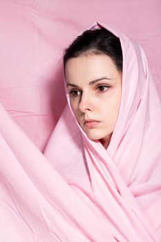 portrait of brunette woman wrapped in pink cloth, pink background. High quality photo