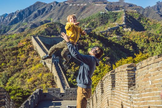 Happy cheerful joyful tourists dad and son at Great Wall of China having fun on travel smiling laughing and dancing during vacation trip in Asia. Chinese destination. Travel with children in China concept.