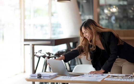 Beautiful Asian businesswoman analyzes charts using laptop calculator at the office..