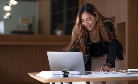 Beautiful Asian businesswoman analyzes charts using laptop calculator at the office..