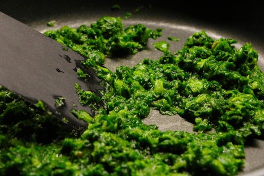 Cook green spinach in a frying pan. Out of focus, blurred