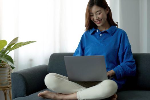 Young business freelance Asian woman working on laptop checking social media while lying on the sofa when relax in living room at home.