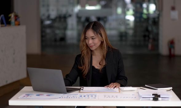 Charming asian businesswoman sitting working on laptop in office..