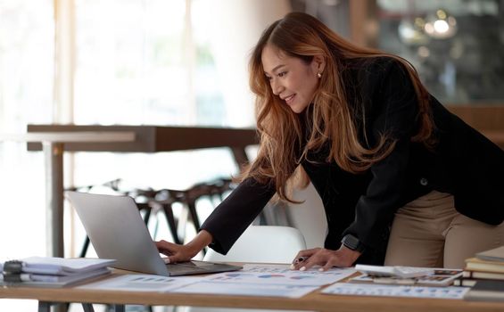 Beautiful Asian businesswoman analyzes charts using laptop calculator at the office..