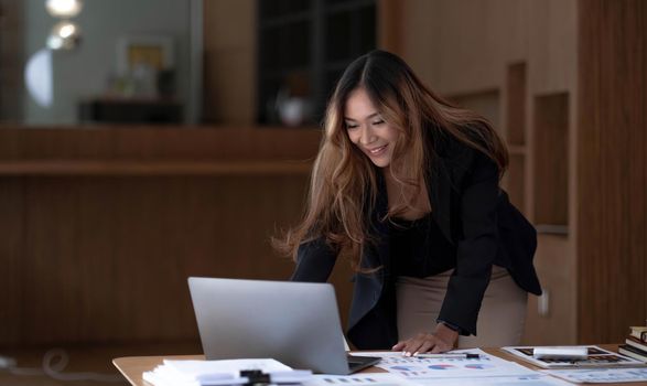 Beautiful Asian businesswoman analyzes charts using laptop calculator at the office..