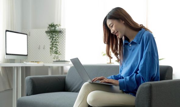 Young business freelance Asian woman working on laptop checking social media while lying on the sofa when relax in living room at home.