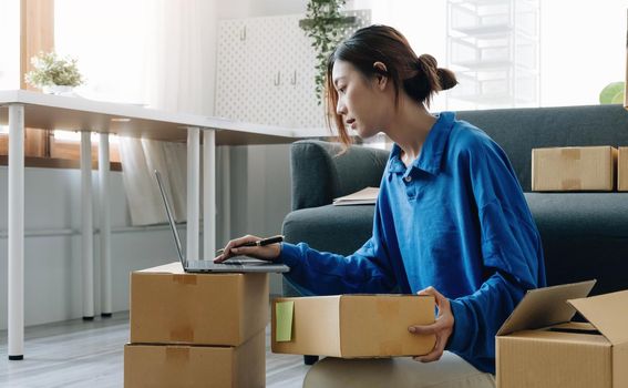 Young asian woman is entrepreneur work from home with online on notebook, online shopping, logistic and delivery, female is seller working on sofa, business SME.
