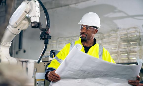 African American factory worker working with adept robotic arm in a workshop . Industry robot programming software for automated manufacturing technology .