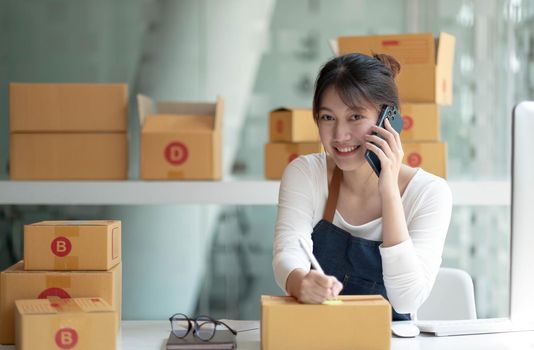 Young Asian small business owner woman hold pen and parcel boxes to write down addresses for delivery to their customers' homes. Looking at camera..
