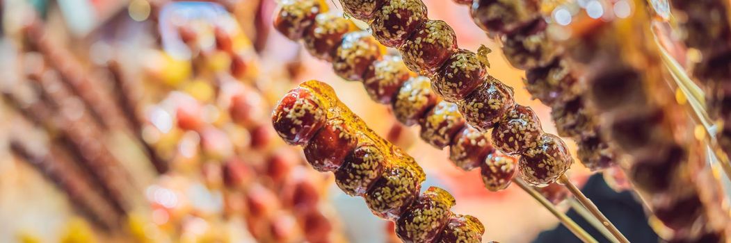 Chinese candied fruits and berries, Hawthorn and strawberries in sesame and sugar syrup. Chinese street food concept. BANNER, LONG FORMAT