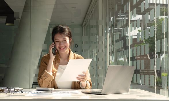 Charming Asian woman with a smile standing holding papers and mobile phone at the office..Charming Asian woman with a smile standing holding papers and mobile phone at the office..