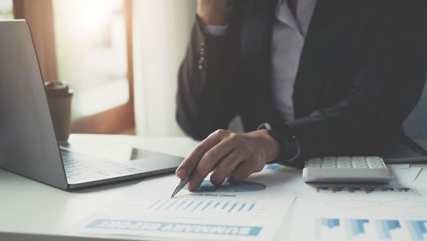 Close up Businesswoman consultant holding pen and pointing at financial on wooden desk in coffee shop. freelance, tax, accounting, statistics and analytic research concept..