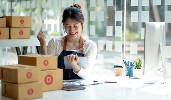 Small business owner wearing an apron is successful selling online using a smartphone parcel box placed at home..