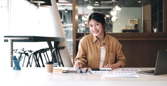 attractive young businesswoman using calculator and smiling at camera while working in office..