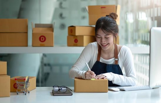 Asian Small business entrepreneur SME writing address on cardboard box at workplace small business entrepreneur SME , working with box at home..