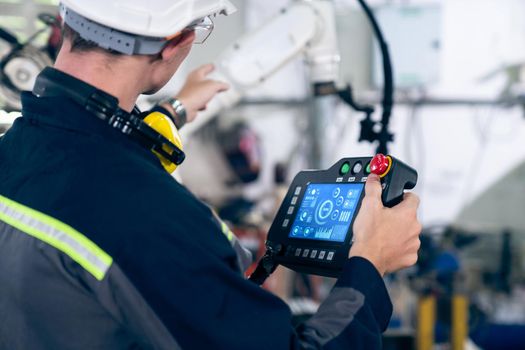 Young factory worker working with adept robotic arm in a workshop . Industry robot programming software for automated manufacturing technology .