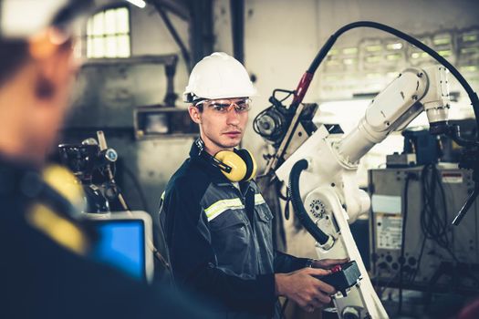 Factory workers working with adept robotic arm in a workshop . Industry robot programming software for automated manufacturing technology .