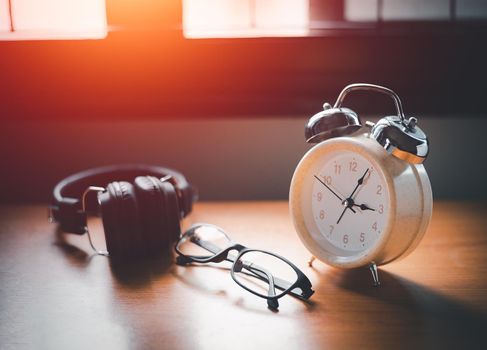 Close-up of retro alarm clock vintage style with Blank,  glasses and headphone on wooden table. Time for Wake up early. light morning through the window.