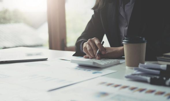 Close up Business woman using calculator and laptop for do math finance on wooden desk in office and business working background, tax, accounting, statistics and analytic research concept.