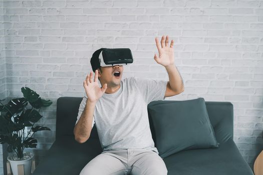 Asian man play VR game for entertain at home, asian man joyful  in house on holiday. Happy man playing metaverse VR technology concept.