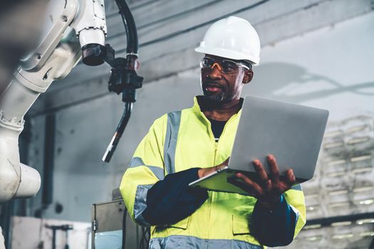 African American factory worker working with adept robotic arm in a workshop . Industry robot programming software for automated manufacturing technology .