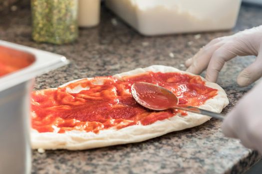 Fresh original Italian raw pizza, dough preparation in traditional style. Applying a tomato sauce.