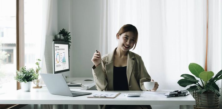Smiling Asian businesswoman holding a coffee mug and laptop at the office. Looking at the camera..