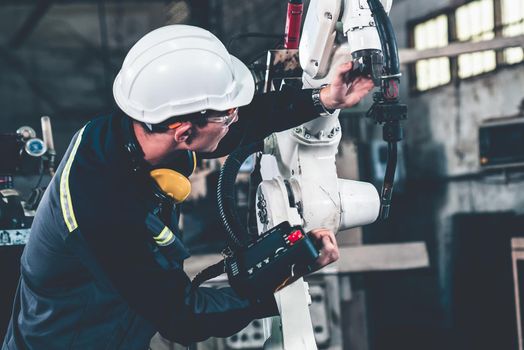 Young factory worker working with adept robotic arm in a workshop . Industry robot programming software for automated manufacturing technology .