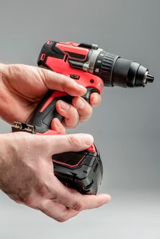 a man's hand removes the battery from a cordless tool. A man inserts a battery into a screwdriver. Repair and construction concept on gray background.