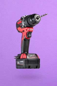 Cordless drill in black and red. Screwdriver with a drill on a purple background. Modern carpentry cordless tool close-up