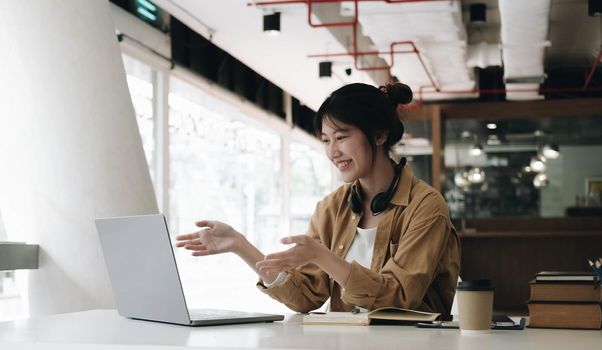 Freelance business women casual wear using laptop working call video conference with customer in workplace in living room at home. Happy young Asian girl relax sitting on desk do job in internet..