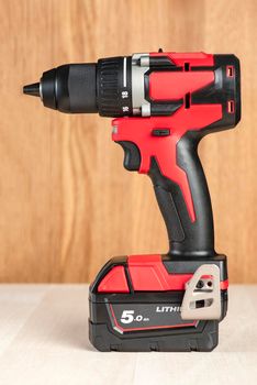 Cordless drill in black and red. A screwdriver with a drill lies on a wooden background. Modern carpentry tool close-up