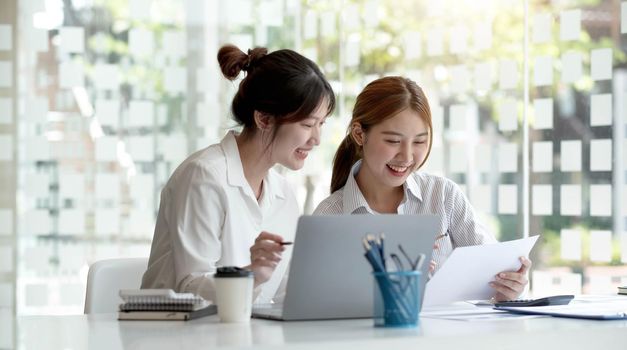 Two young Asian businesswoman discuss investment project working and planning strategy. Business people talking together with laptop computer at office..