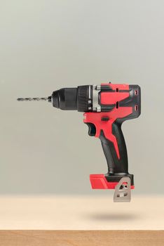 Wireless tools. Cordless drill with drill bit. The screwdriver with the battery removed falls, casting a shadow. Advertising banner of construction or industrial theme on wooden background.