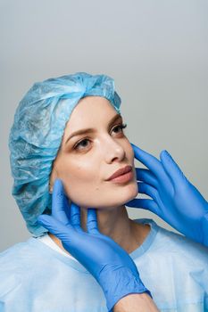 Consultation with plastic surgeon on white background. Cosmetic rejuvenating facial treatment. Doctor man with blue medical gloves touches girl face.