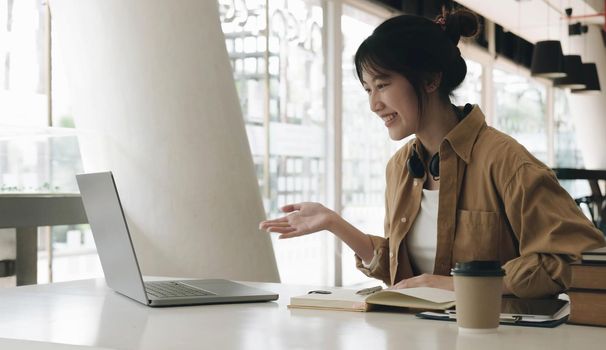 Freelance business women casual wear using laptop working call video conference with customer in workplace in living room at home. Happy young Asian girl relax sitting on desk do job in internet..