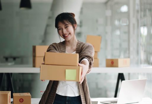 Happy young asian woman startup small business freelance holding parcel box and computer laptop. Online marketing packing box delivery concept.