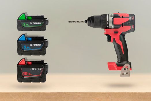 Batteries for cordless tools. Batteries for a screwdriver of different capacities and different sizes. Electric drill and three batteries with a charge indicator on a wooden background.