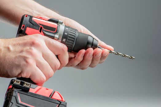 The man's hands install the drill into the drill, the hands take the drill and install it into the electric drill. Cordless tool on a gray background