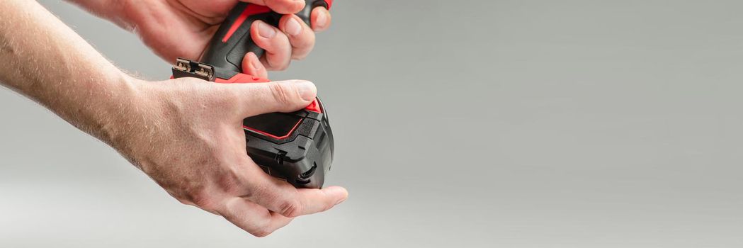 a man's hand removes the battery from a cordless tool. A man inserts a battery into a screwdriver. Repair and construction concept on gray background.