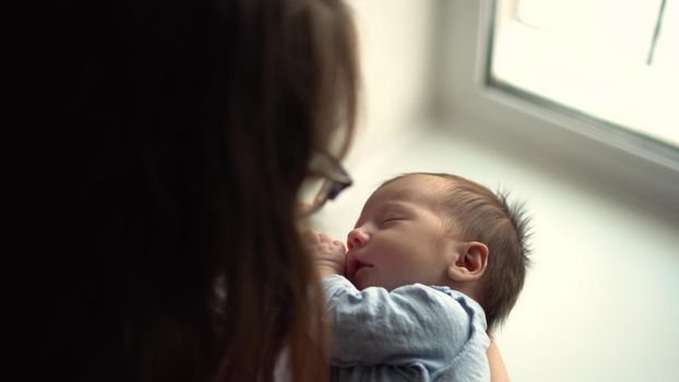 A young mother holds a child in her arms against the background of a window. View from above. 4k