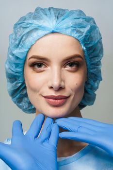 Consultation with plastic surgeon on white background. Cosmetic rejuvenating facial treatment. Doctor man with blue medical gloves touches girl face.