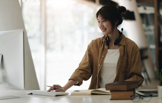 Young Asian woman wearing headphones is using a laptop at home..