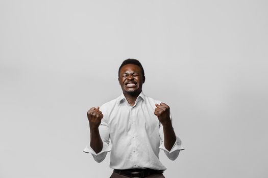 Happy handsome black man wins online bet on white background. Shouting loud Yes and making crazy emotions. African won a prize. Online work at home